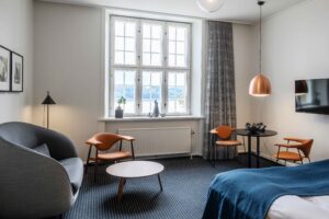 Mørkeblåt gulvtæppe i hotelværelse med grå og blå farver på seng og møbler